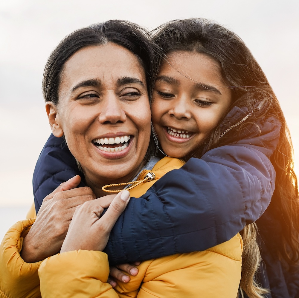 Happy latin mother and daughter having fun together on the beach during winter time - Focus on girl face Happy latin mother and daughter having fun together on the beach during winter time - Focus on girl face